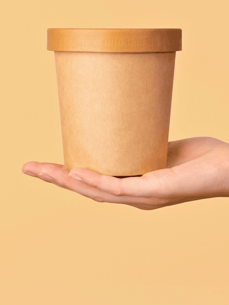 A hand holding a paperboard takeaway containers against a yellow background.