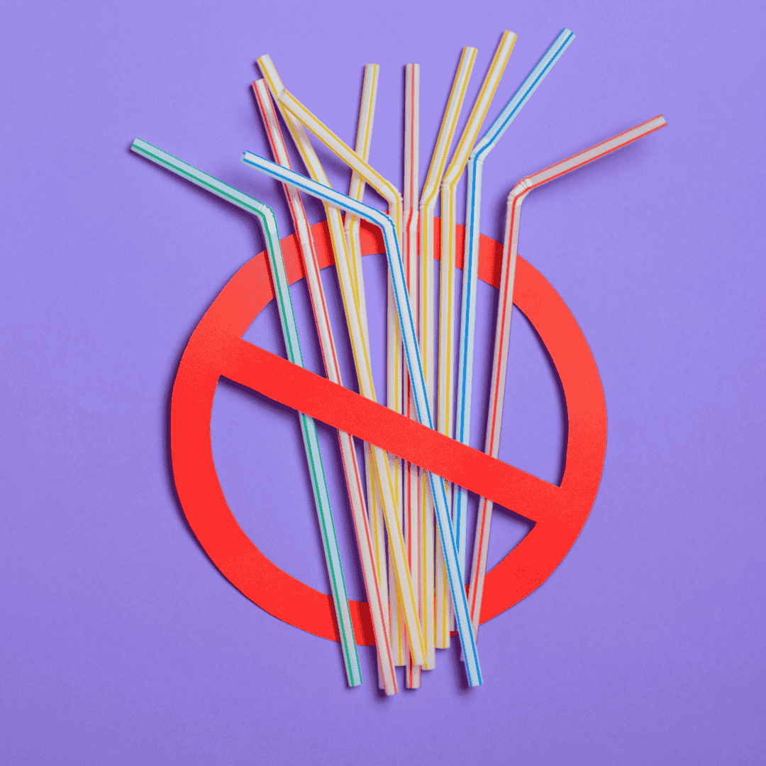 Colourful plastic straws positioned over a red banned symbol on a purple background.