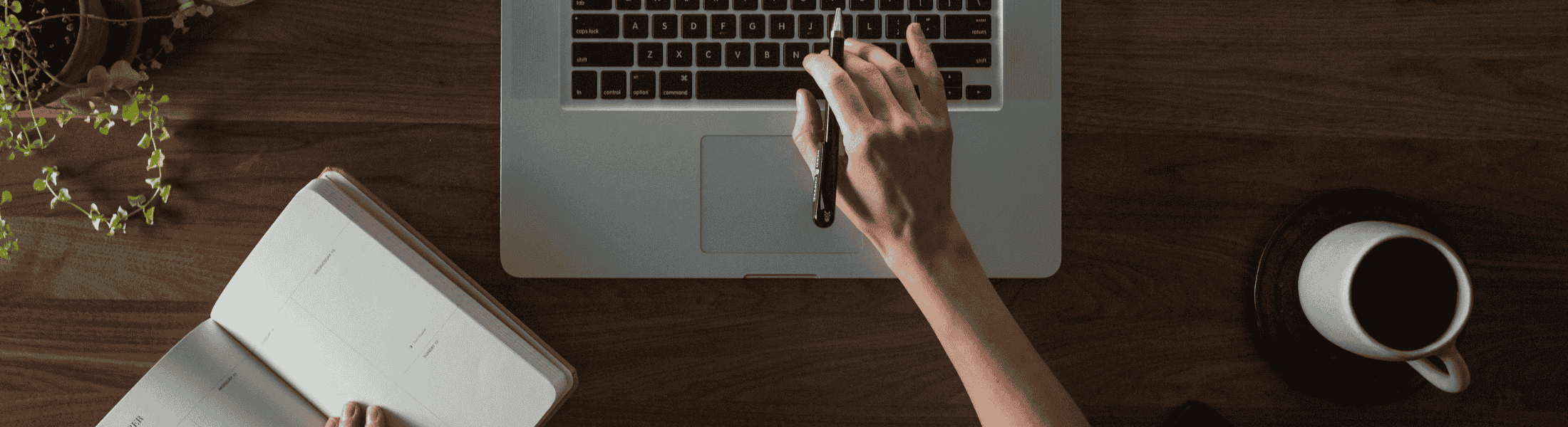 A person types on a laptop with a cup of coffee beside them.
