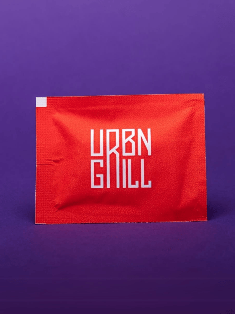 A red wet wipe packet with white text reading URBN GRILL on a purple background.